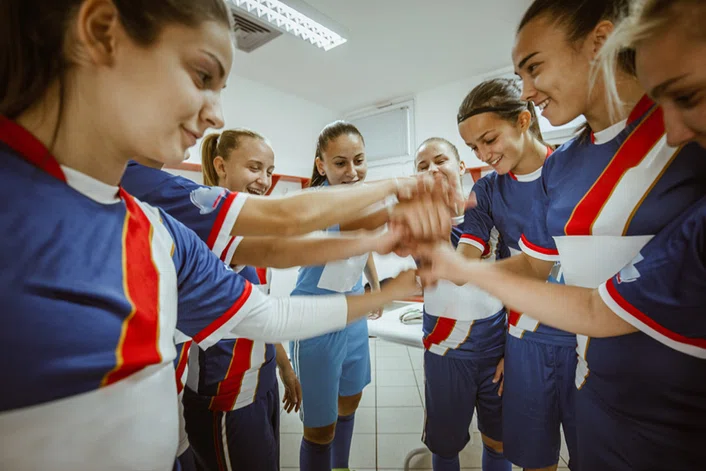 Girls soccer team putting hands together in supportive huddle.