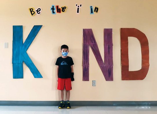 A boy in a mask stands as the I in the word KIND.