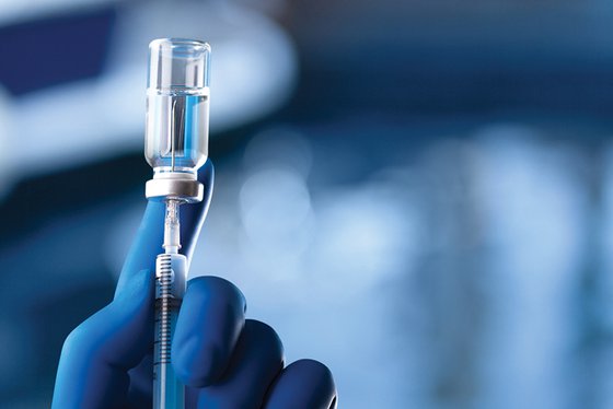 Gloved hand holding needle in a bottle of vaccine.